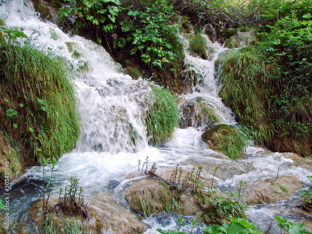 Top view of falling water into a crystal clear lake on a mountain slope richly covered with tall grass. Top view of falling water into a crystal clear lake on a mountain slope richly covered with tall grass.