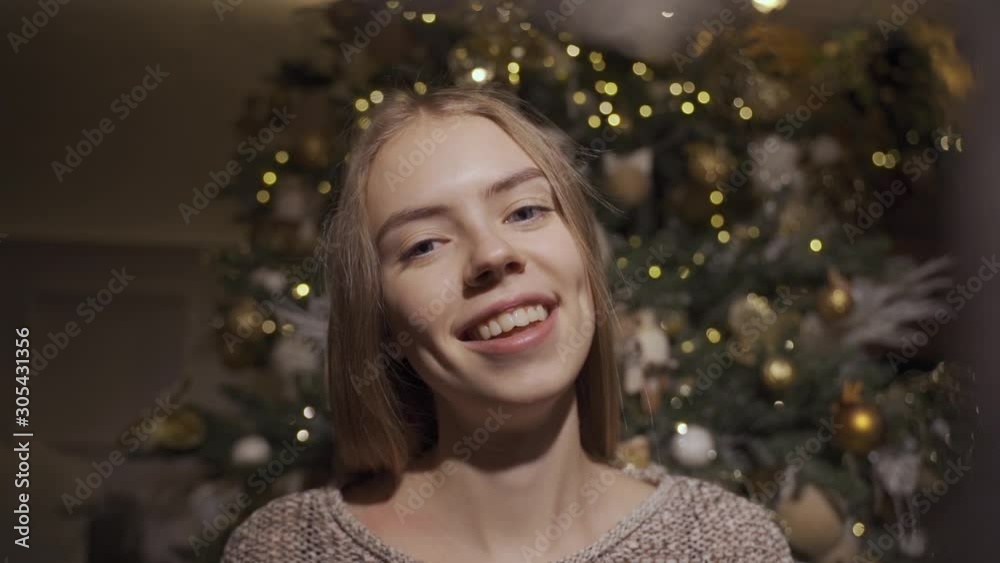 A young pretty girl smiles and opens a Christmas present. Girl opens a gift on the background of a Christmas tree A young pretty girl smiles and opens a Christmas present. Girl opens a gift on the background of a Christmas tree