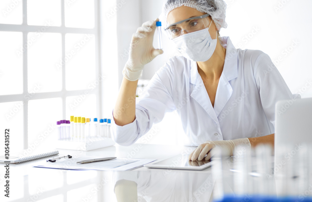 Professional female scientist in protective eyeglasses researching tube with reagents in laboratory. Concepts of medicine and research Professional female scientist in protective eyeglasses researching tube with reagents in laboratory. Concepts of medicine and research