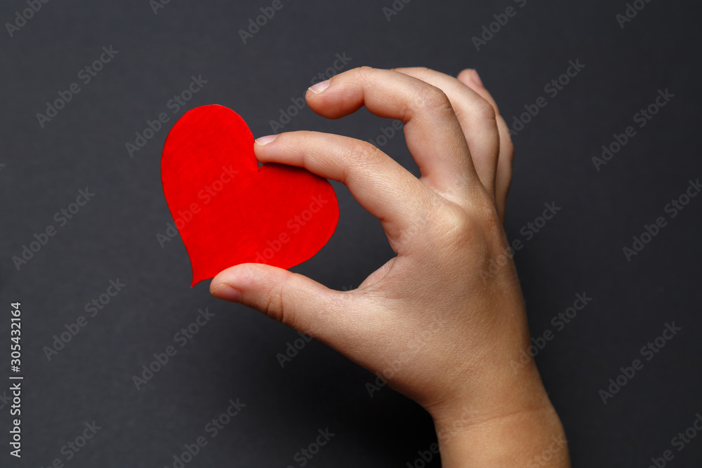 Fototapeta premium Children's hands hold a red heart on a black background, healthcare, love, organ donation, family insurance and CSR concept, World Heart Day, World Health Day, World Volunteer Day.