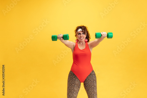 Young caucasian plus size female model's training on yellow background. Copyspace. Concept of sport, healthy lifestyle, body positive, fashion, style. Flexible woman with weights, looks stylish. © master1305