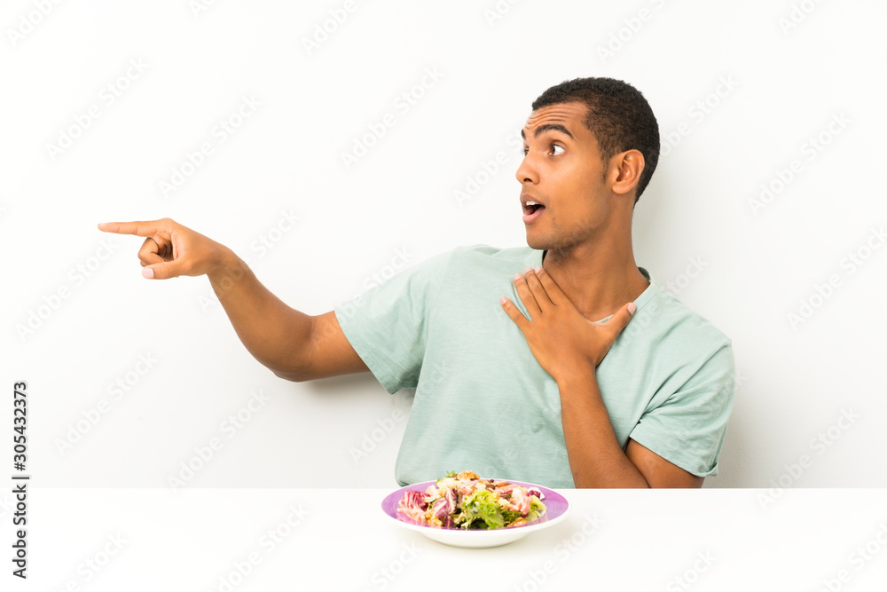 Young handsome man with salad in a table pointing finger to the side Young handsome man with salad in a table pointing finger to the side