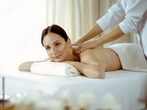 Pretty brunette woman enjoying procedure of back massage in spa salon. Beauty concept