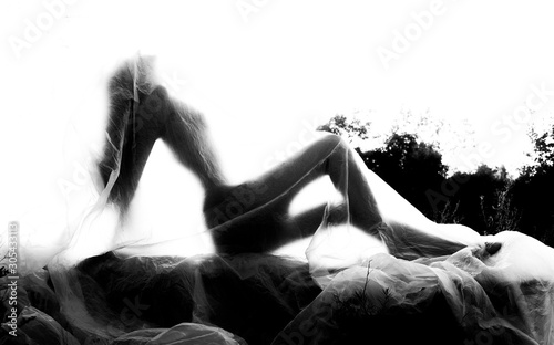 Slender nude girl, covered by a cellophane film, through which only her silhouette is visible and her nakedness is covered, in the ruins of a destroyed building. Conceptual, artistic, creative design.