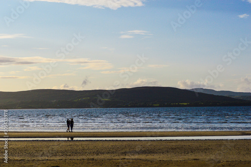 Couple Walking on Beach with Sunset Reflection on the Sea. Blue Sky & Cloud at Background