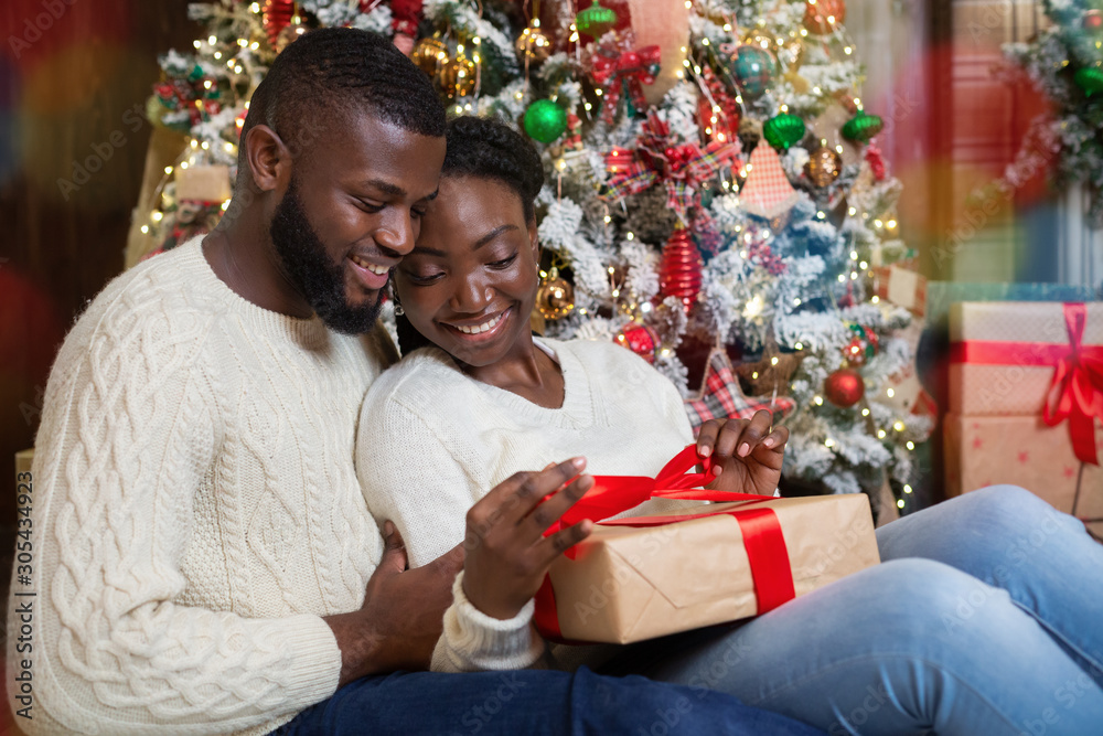 Happy afro woman opening Christmas gift from her caring husband