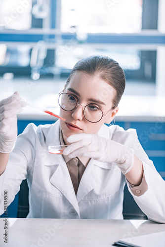 selective focus of beautiful immunologist holding pipette with red liquid in laboratory