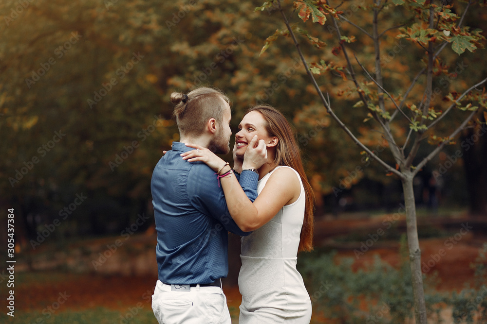 Fototapeta premium Cute couple in a park. Lady in a white dress. Man in a blue shirt