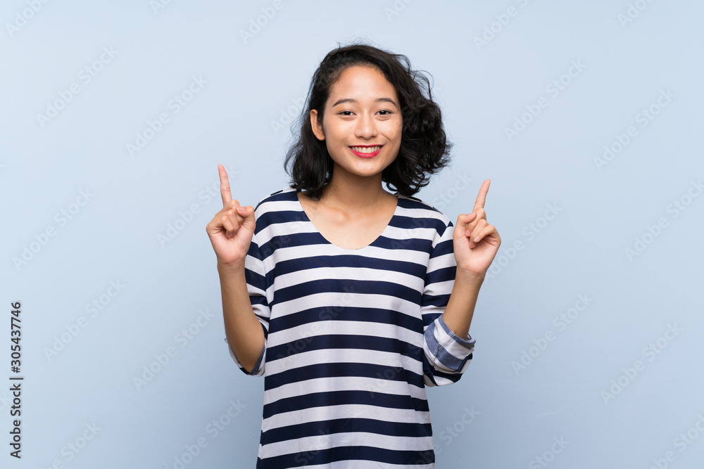 Asian young woman over isolated blue background pointing up a great idea Asian young woman over isolated blue background pointing up a great idea