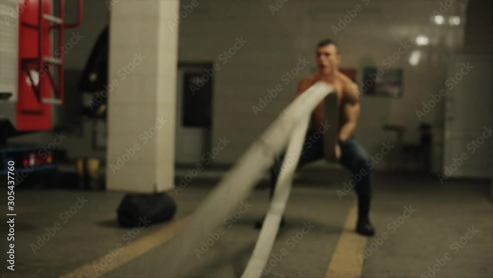Attractive shirtless fireman works out using two fire hoses as battle ropes