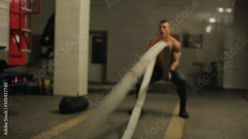 Attractive shirtless fireman works out using two fire hoses as battle ropes