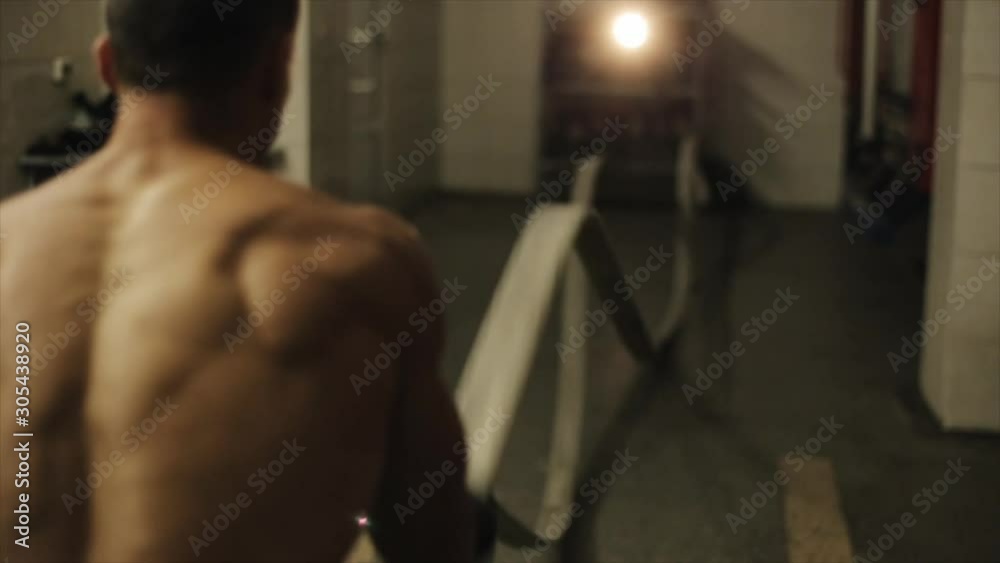 Close rear view of muscular fireman exercising holding two unfold fire hoses and moving hands fast Close rear view of muscular fireman exercising holding two unfold fire hoses and moving hands fast