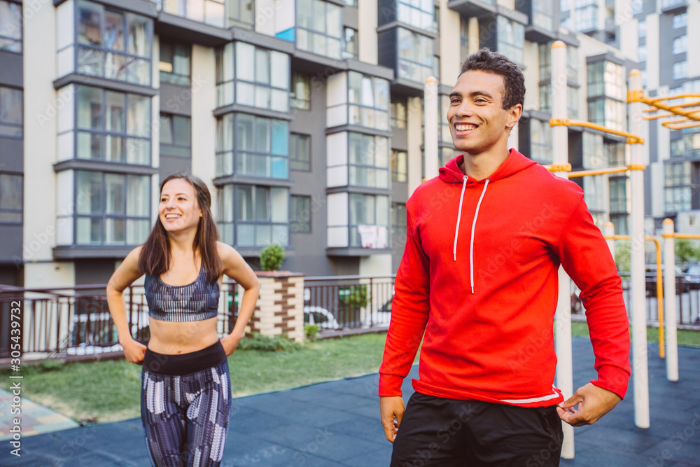 Fototapeta premium Young couple in black sports outfit doing morning workout outdoors. Young man and woman stretching they muscle before running on bridge.