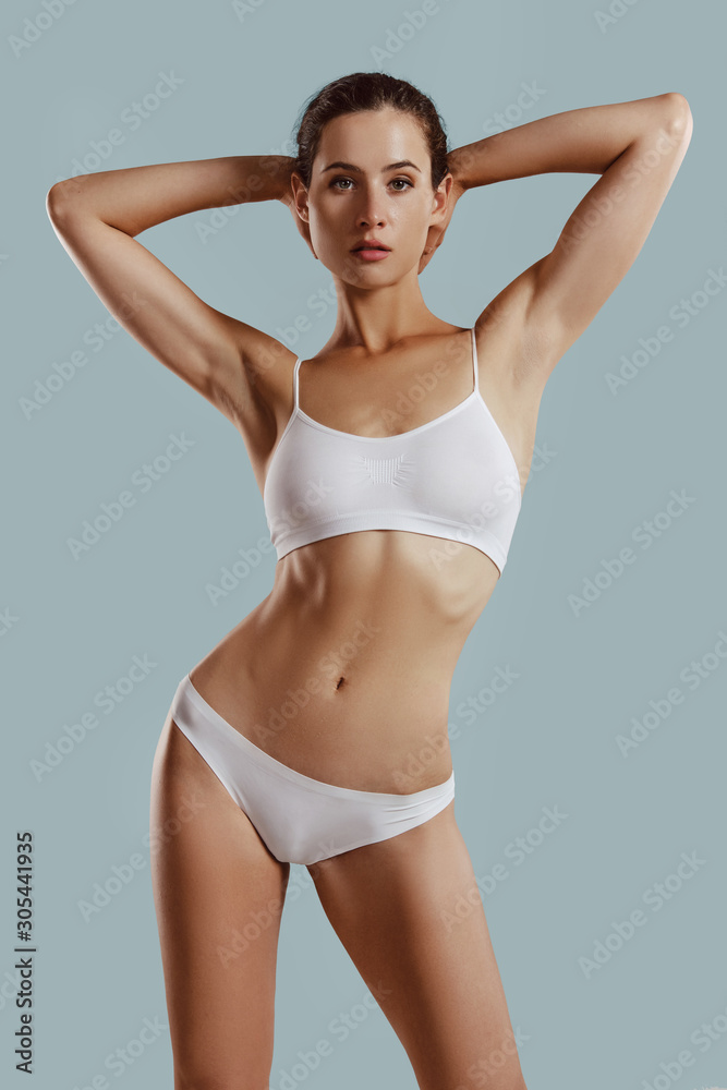 Young woman in white underwear, with bundled hair, put hands on head, posing on gray background. Plastic surgery, aesthetic cosmetology. Close-up. Young woman in white underwear, with bundled hair, put hands on head, posing on gray background. Plastic surgery, aesthetic cosmetology. Close-up.