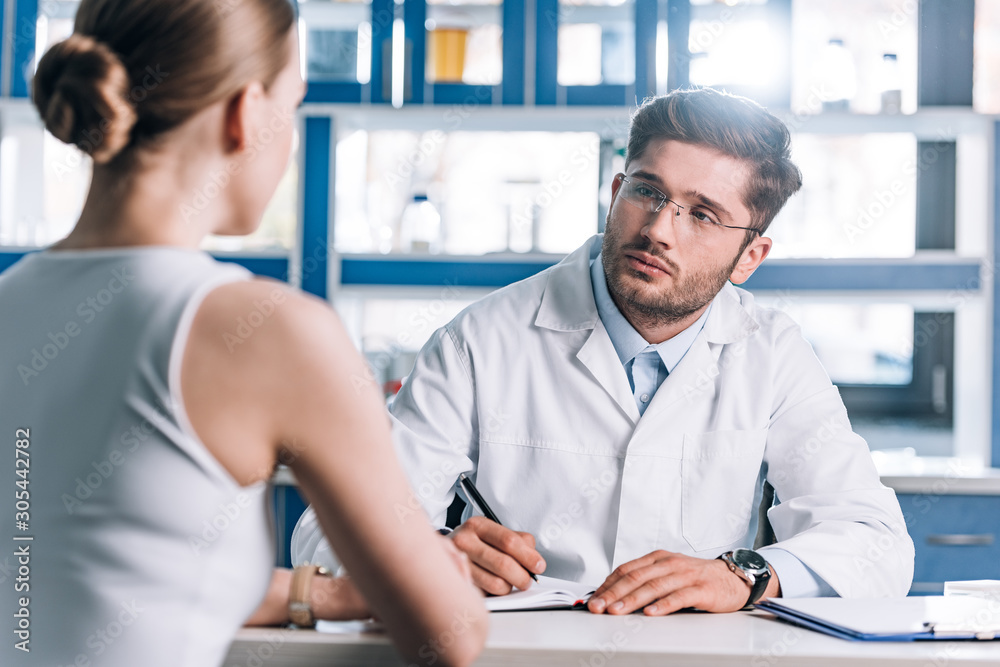 Fototapeta premium selective focus of handsome doctor holding pen and looking at patient