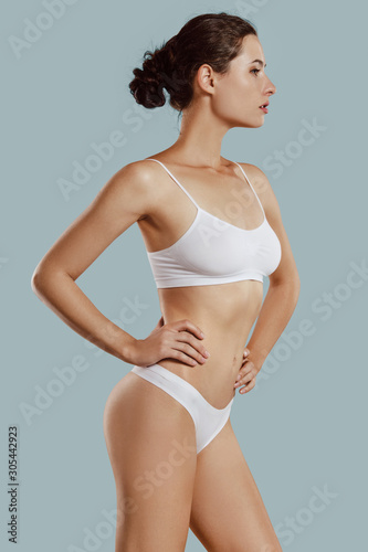 Young woman in white underwear, with bundled hair, posing in studio against gray background. Plastic surgery, aesthetic cosmetology. Close-up.