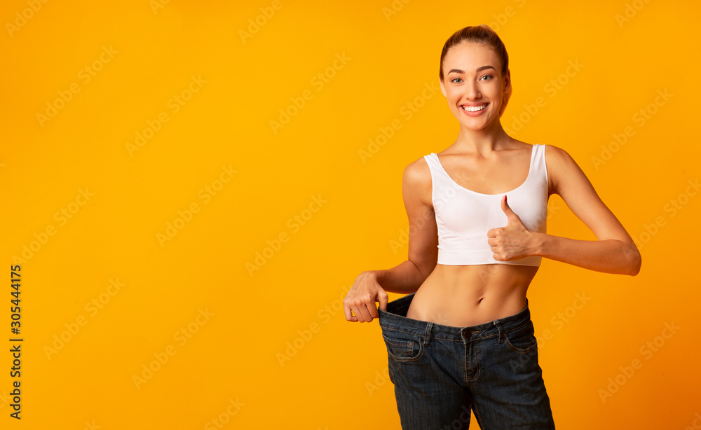 Girl In Oversize Jeans Gesturing Thumbs Up Smiling, Yellow Background - obrazy, fototapety, plakaty 