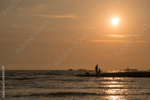 Beautiful sunset nature background, unknown fisherman with net fish on beach. Father and son fishing. Family bond concept.