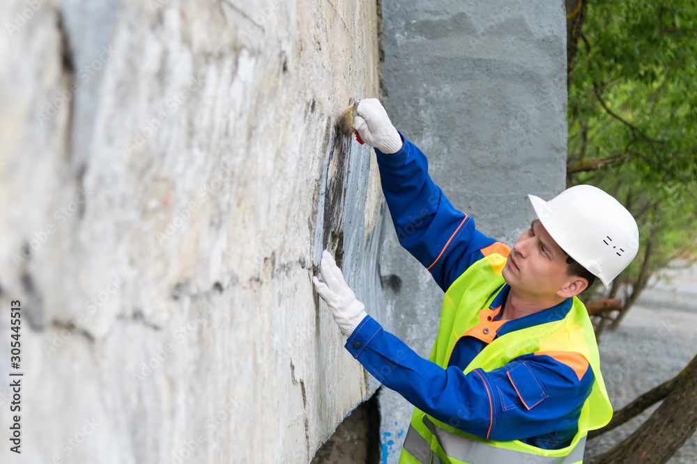 a worker in a helmet cleans vandal inscriptions from the walls in the city