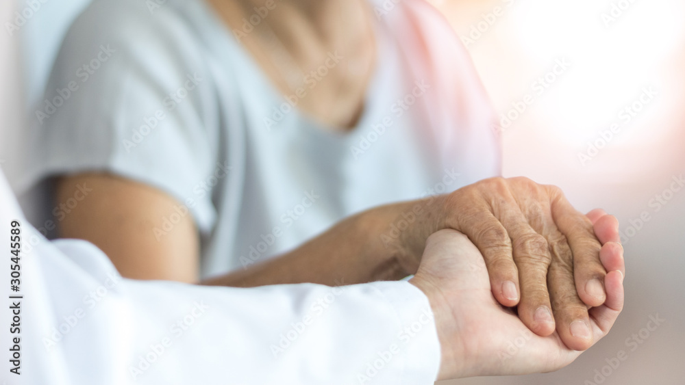 Elderly female hand holding hand of young caregiver at nursing home.Geriatric doctor or geriatrician concept. Doctor physician hand on happy elderly senior patient to comfort in hospital examination - obrazy, fototapety, plakaty 
