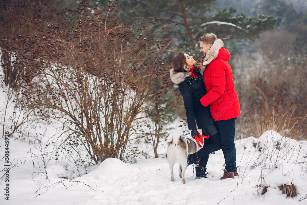 Cute couple in a winter park. Woman palying with a dog. Lady in a black jacket