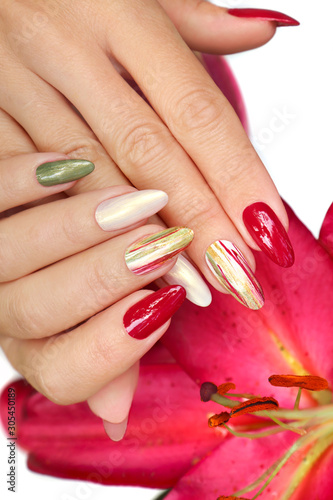 Multicolored manicure on long nails oval with mother of pearl shiny nail Polish on the background of lilies.