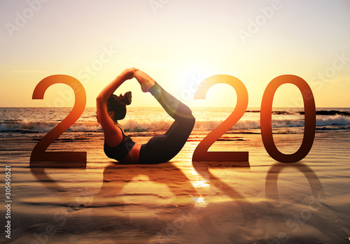 Happy new year card 2020. Silhouette of healthy girl doing Yoga Bow pose on tropical beach with sunset sky background, woman practicing yoga as a part of the Number 2020 sign.