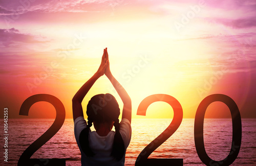 Happy new year card 2020. Silhouette of girl doing Yoga vrikshasana tree pose on tropical sea with fantastic sunset sky background. Kid standing as part of the Number 2020 sign and watching sunrise.