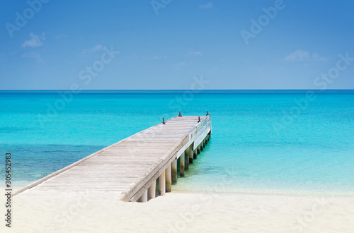 Wooden bridge or pier on tropical white sand beach with clear blue sea and sky on sunny day. Boardwalk into the ocean and turquoise water. Summer holidays background with copy space. Kuramathi Island.