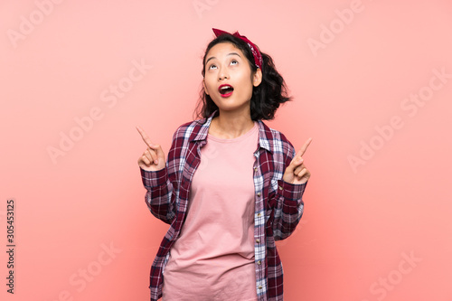 Asian young woman over isolated pink background surprised and pointing up