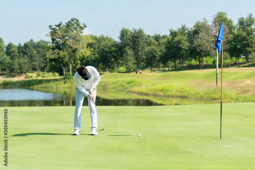 Obraz premium Professional Golfer asian man playing aiming shot for putting ball on the hole with club on green course. Hobby in holiday and vacations in sunny morning day on club golf. Lifestyle and Sport Concept