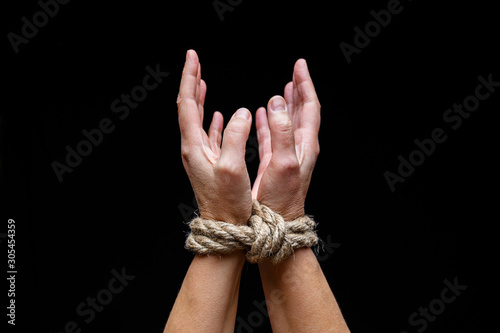 Woman with tied hands. Hands tied with rope on dark background. International Day for the Elimination of Slavery.