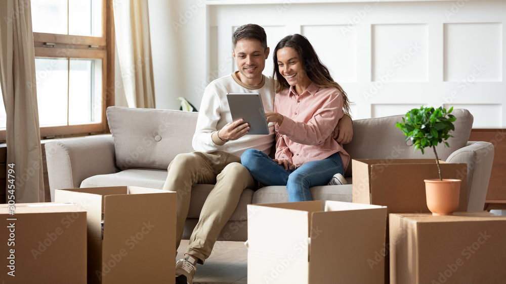 Happy couple using digital tablet sit on sofa with boxes Happy couple using digital tablet sit on sofa with boxes