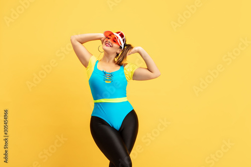 Young caucasian plus size female model's training on yellow background. Copyspace. Concept of sport, healthy lifestyle, body positive, fashion, style. Stylish woman chilling, resting and smiling.