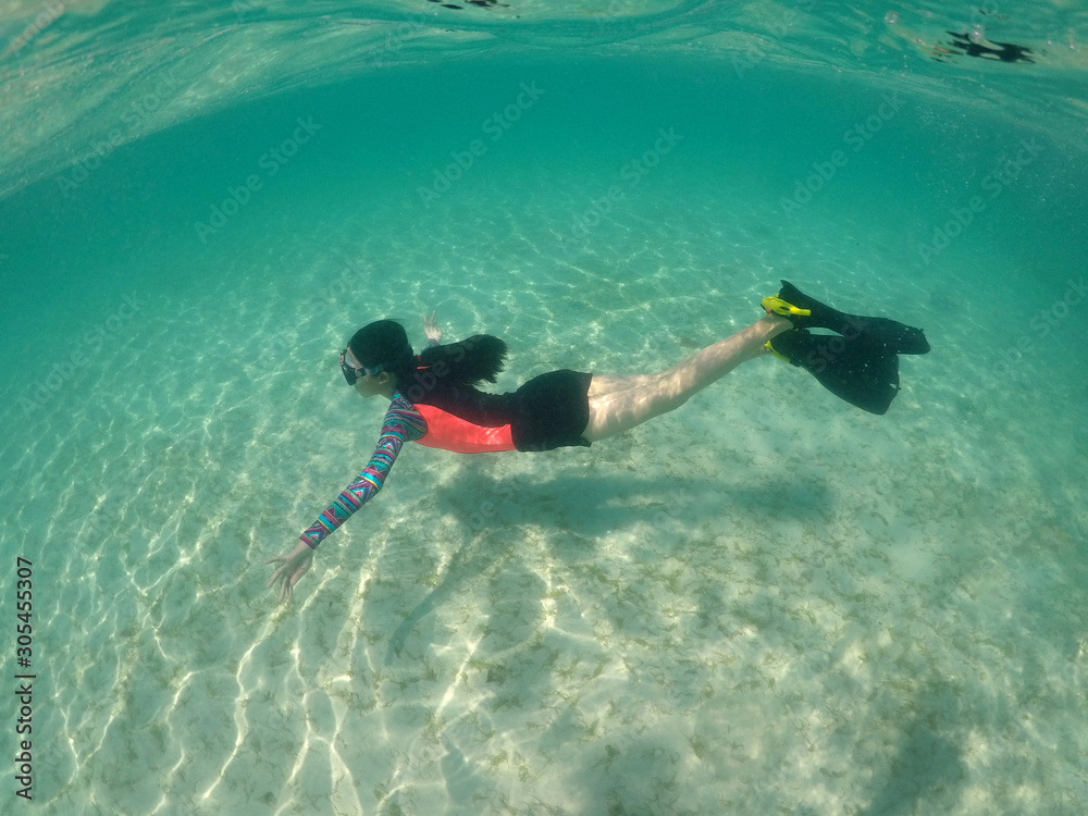 Asian teenager girl enjoy summer vacation on sunny day in crystal clear water. Half underwater of young  healthy woman in colorful swimsuit, mask and black fins relaxing, free diving on turquoise sea.