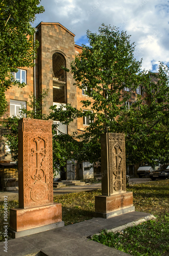   Red and grey stone khachkars with carved tracery and crosses standing side by side on the Alley of stone crosses in Gyumri