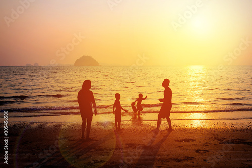 Silhouette of happy family of four people, mother, father, daughter and son enjoy at sunset beach. Dad, mom and children playing on the beach. Concept of friendship forever and  summer vacation time.