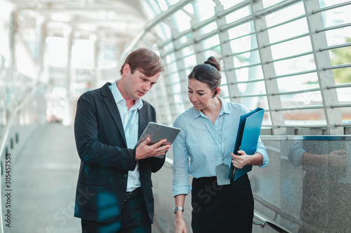 Business couples are discussing business issues while walking on the skywalk Both are busy working all day. And still holding the file with the tablet all the time