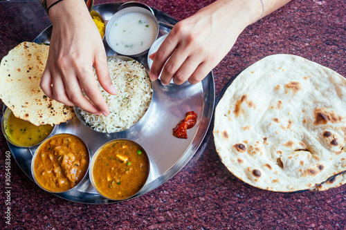 close up photo of Indian traditional vegetarian thali from rice, dal, potatoes, tomato salad on metal plate ,female hands roti india tortilla Chapati photo