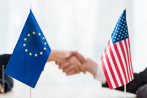 selective focus of flags of usa and european union near diplomats shaking hands photo