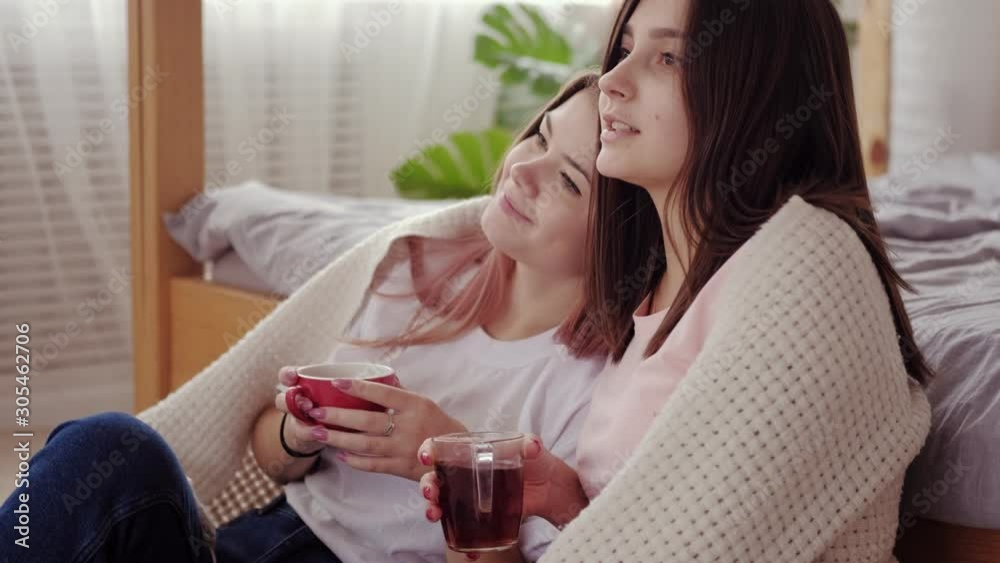 Sisters leisure. Family bonding. Two happy teen girls enjoying hot drinks watching movie together. Sisters leisure. Family bonding. Two happy teen girls enjoying hot drinks watching movie together.