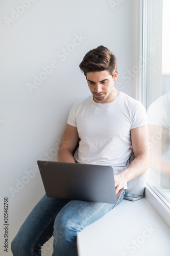 Handsome man working on a windowsill with a laptop, worker communicating on the Internet.