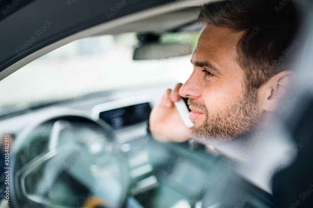 Young businessman with smartphone sitting in car, making phone call.