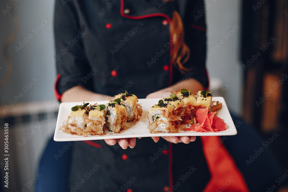 Woman holds sushi. It happens indoors. Sushi are on white plate.