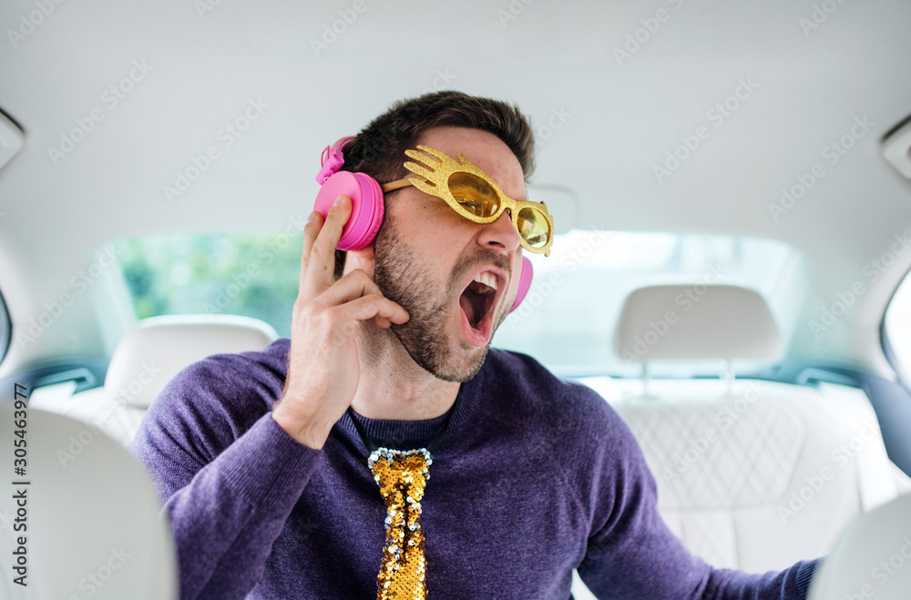 Cheerful man with party accessories sitting in car, having fun. - obrazy, fototapety, plakaty 