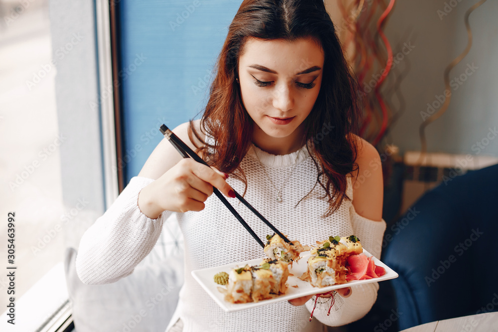 Woman holds chopsticks in her hands. She holds a plate with sushi. Woman is sitting in cafe.