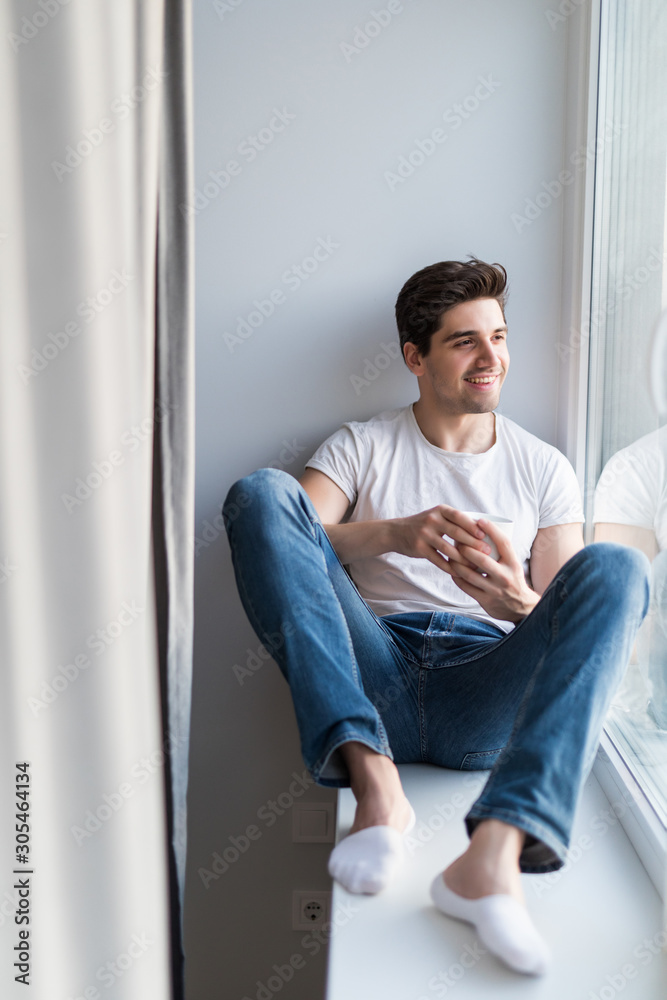 Handsome man sitting at window sill and drinking morning coffee Handsome man sitting at window sill and drinking morning coffee