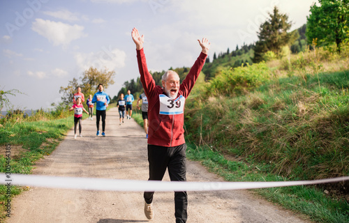 Senior man runner crossing finish line in a race competition in nature.