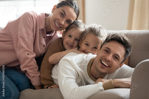 Happy family of four bonding on sofa looking at camera