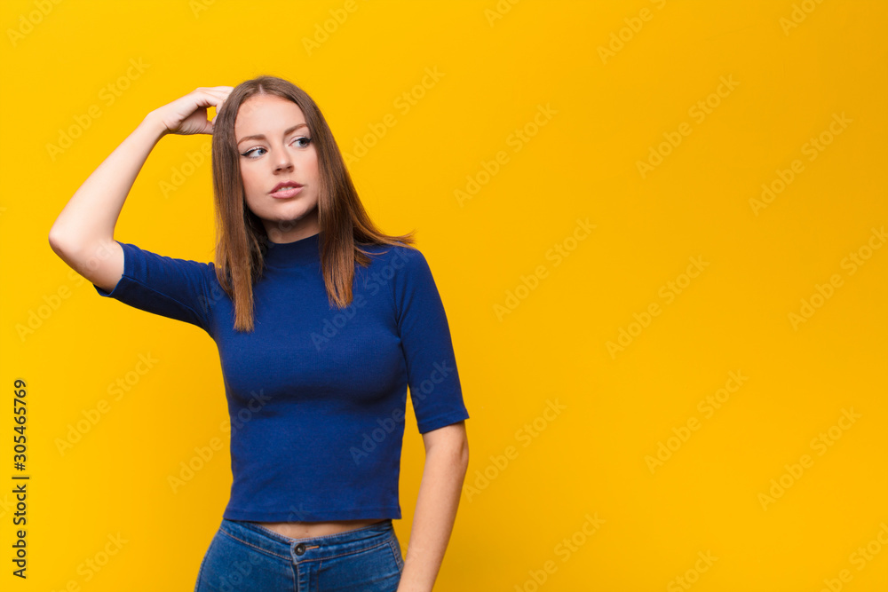young red head woman feeling puzzled and confused, scratching head and  looking to the side against flat wall Stock Photo | Adobe Stock